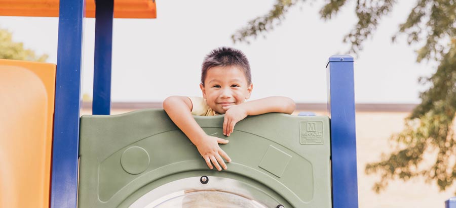 Boy hanging over playground equipment smiling