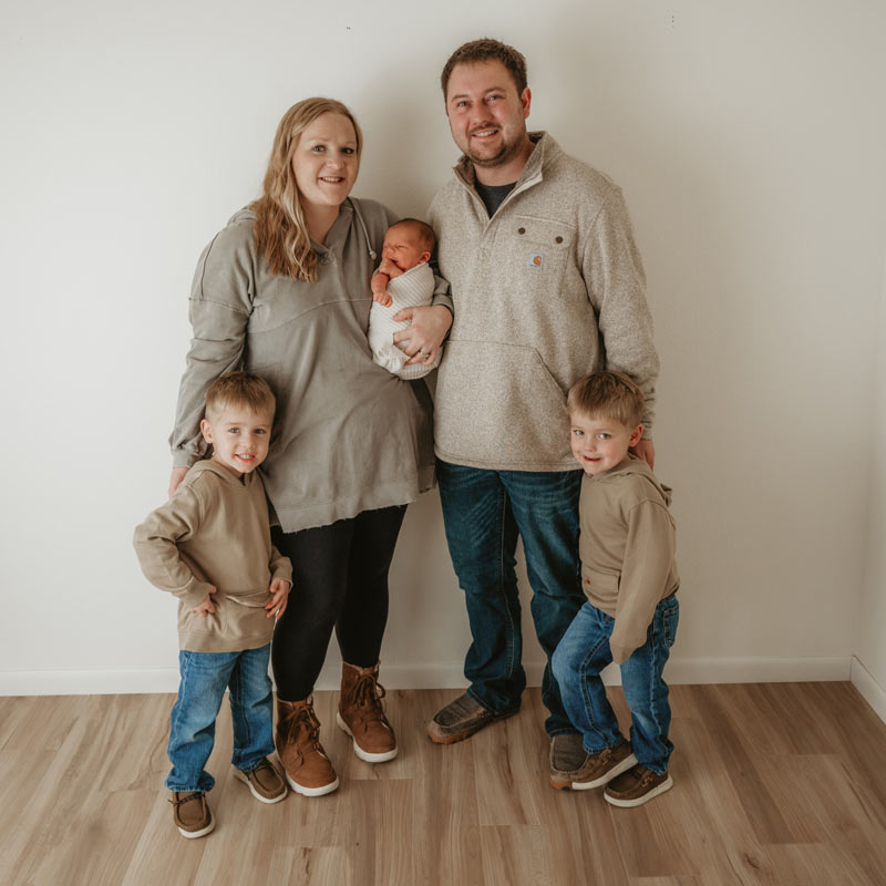 Maday Family of two parents, two boys and one baby standing in front of a wall